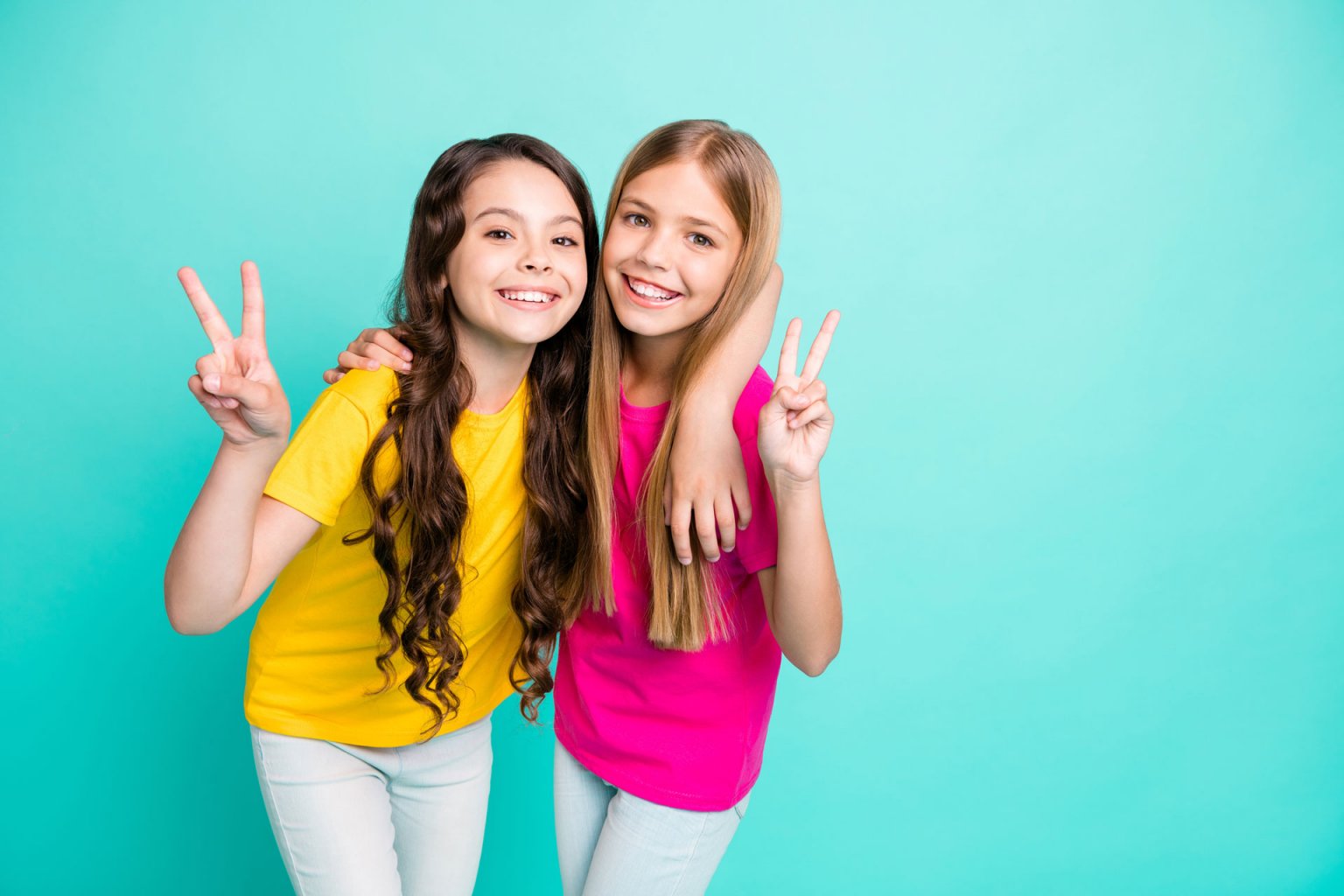 Two Excited Cheerful Teen Girls Hugging Like Best Friends And Holding Up Two Fingers As The